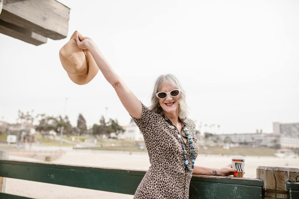 Older woman posing for a photo holding a coffee and her hat